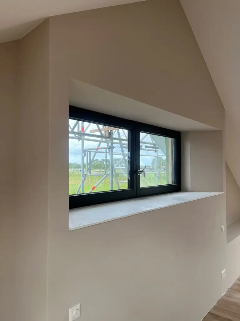 Glad gestucte wand met diepe raamnis en zwart kozijn